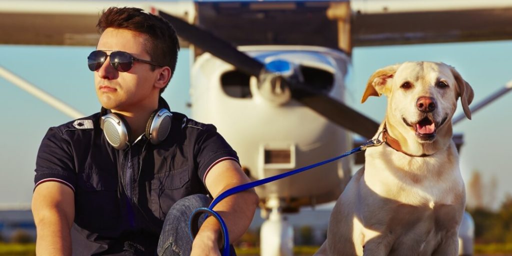 a man sitting with a dog in-front of a plane